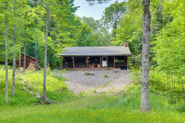 A cabin with a porch, surrounded by trees and a gravel path. - Waterfront Cottage w/ Dock on Papoose Lake! (Manitowish Waters)
