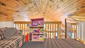 A loft-style room with a high ceiling and exposed wooden beams. It features a multi-level dollhouse, a sofa, and a staircase. - Waterfront Cottage w/ Dock on Papoose Lake! (Manitowish Waters)