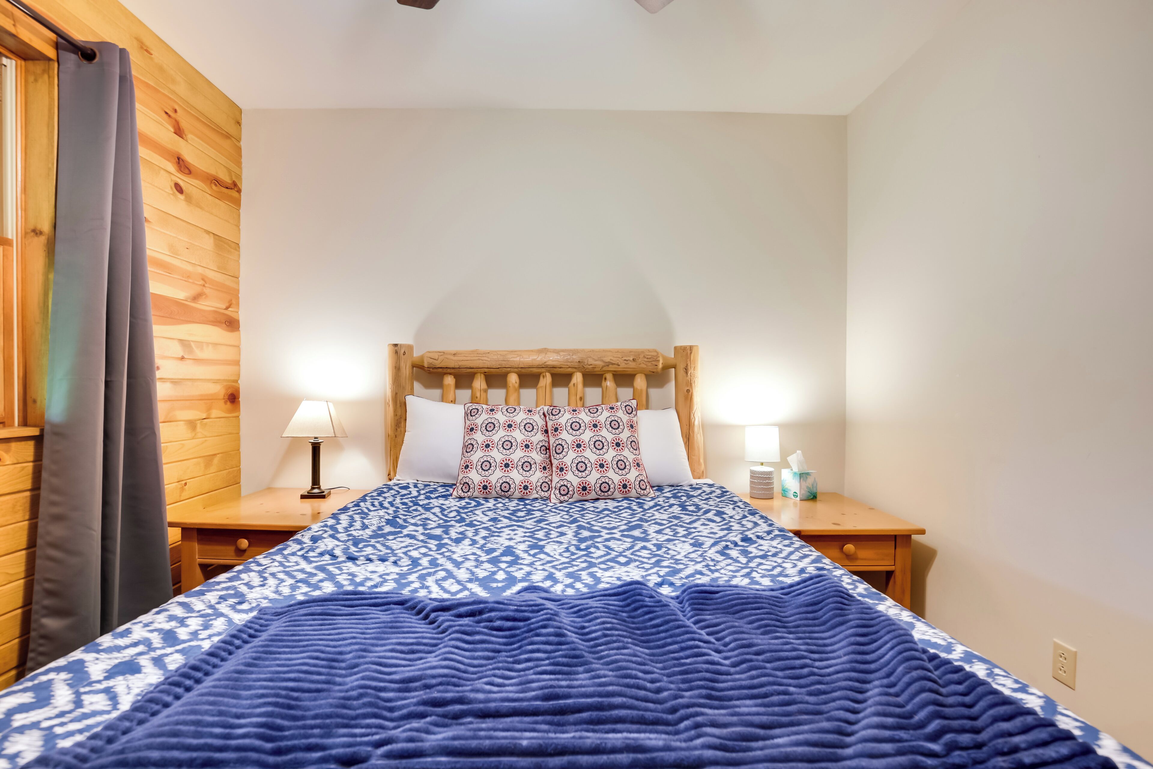 Une chambre à coucher avec une tête de lit en bois, une couvre-lit à motifs, deux lampes de chevet et une table de chevet sur laquelle se trouve une boîte à mouchoirs.