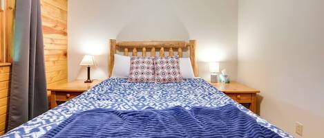 Une chambre à coucher avec une tête de lit en bois, une couvre-lit à motifs, deux lampes de chevet et une table de chevet sur laquelle se trouve une boîte à mouchoirs.