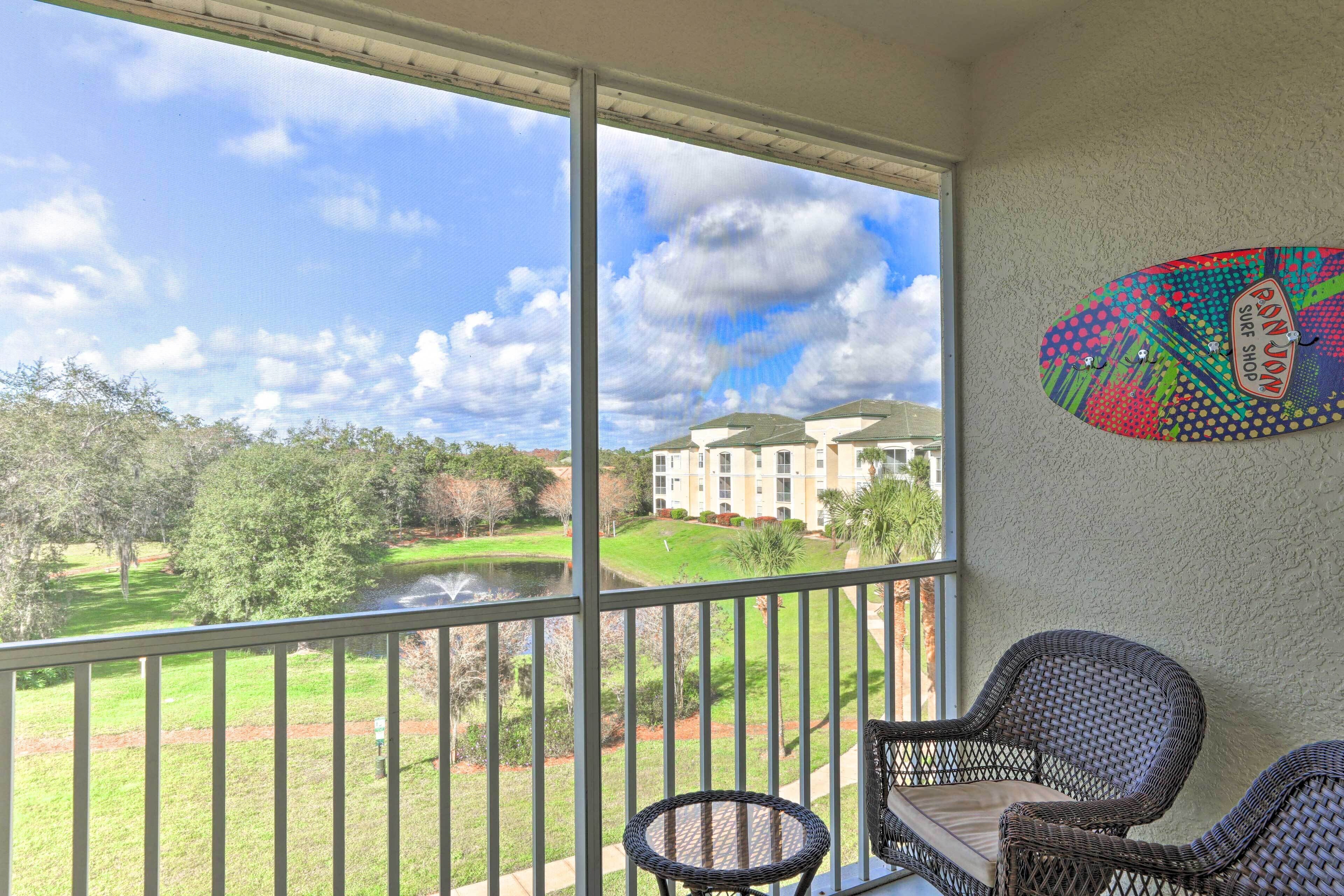 Een balkon met rieten meubels, uitzicht op een golfbaan, en een gebouw op de achtergrond.