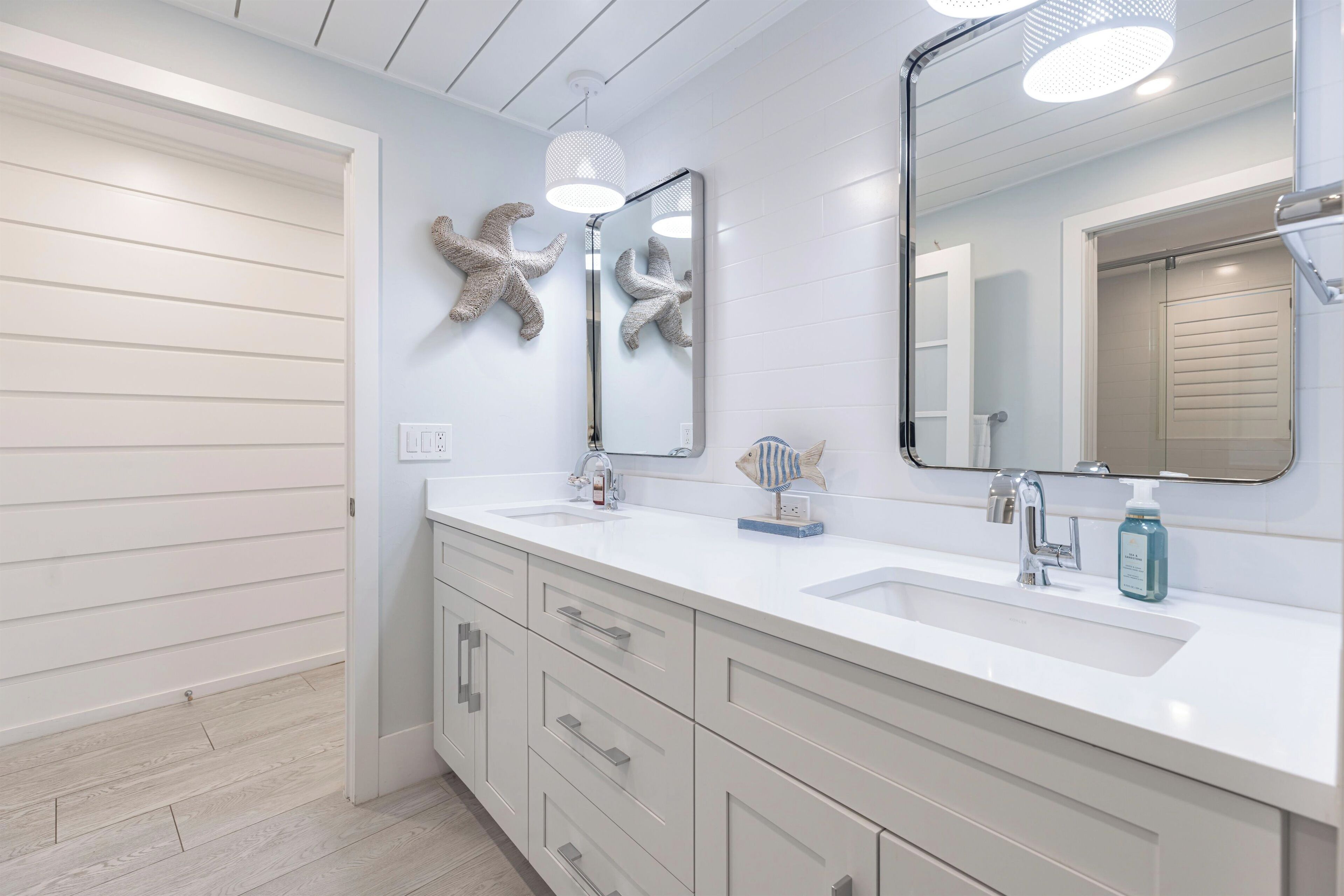 Une salle de bain moderne avec deux vasques, un grand miroir et des décorations murales représentant des étoiles de mer.