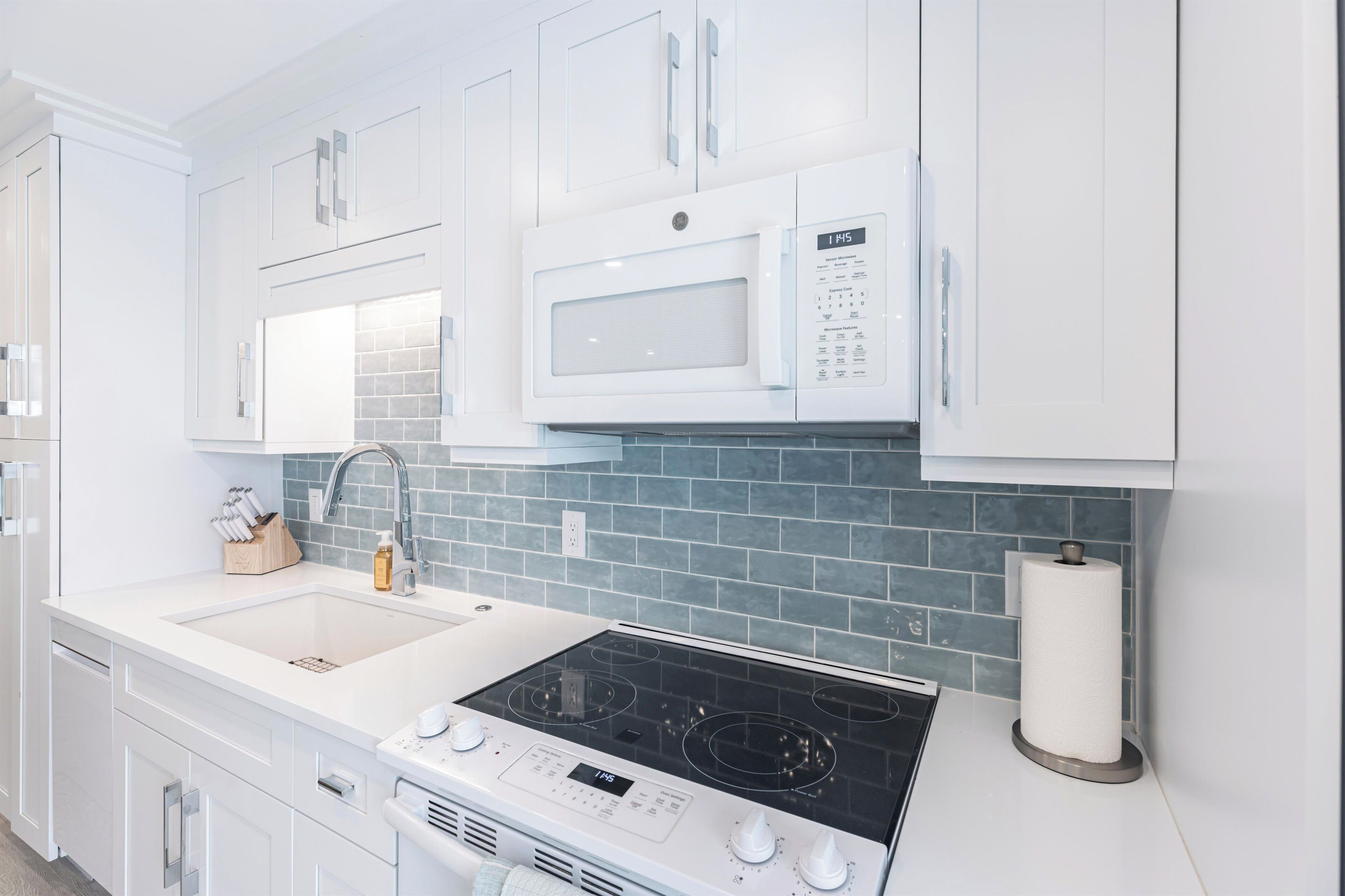 A modern kitchen with white cabinetry, a built-in microwave, a gas stove, and a tiled backsplash.