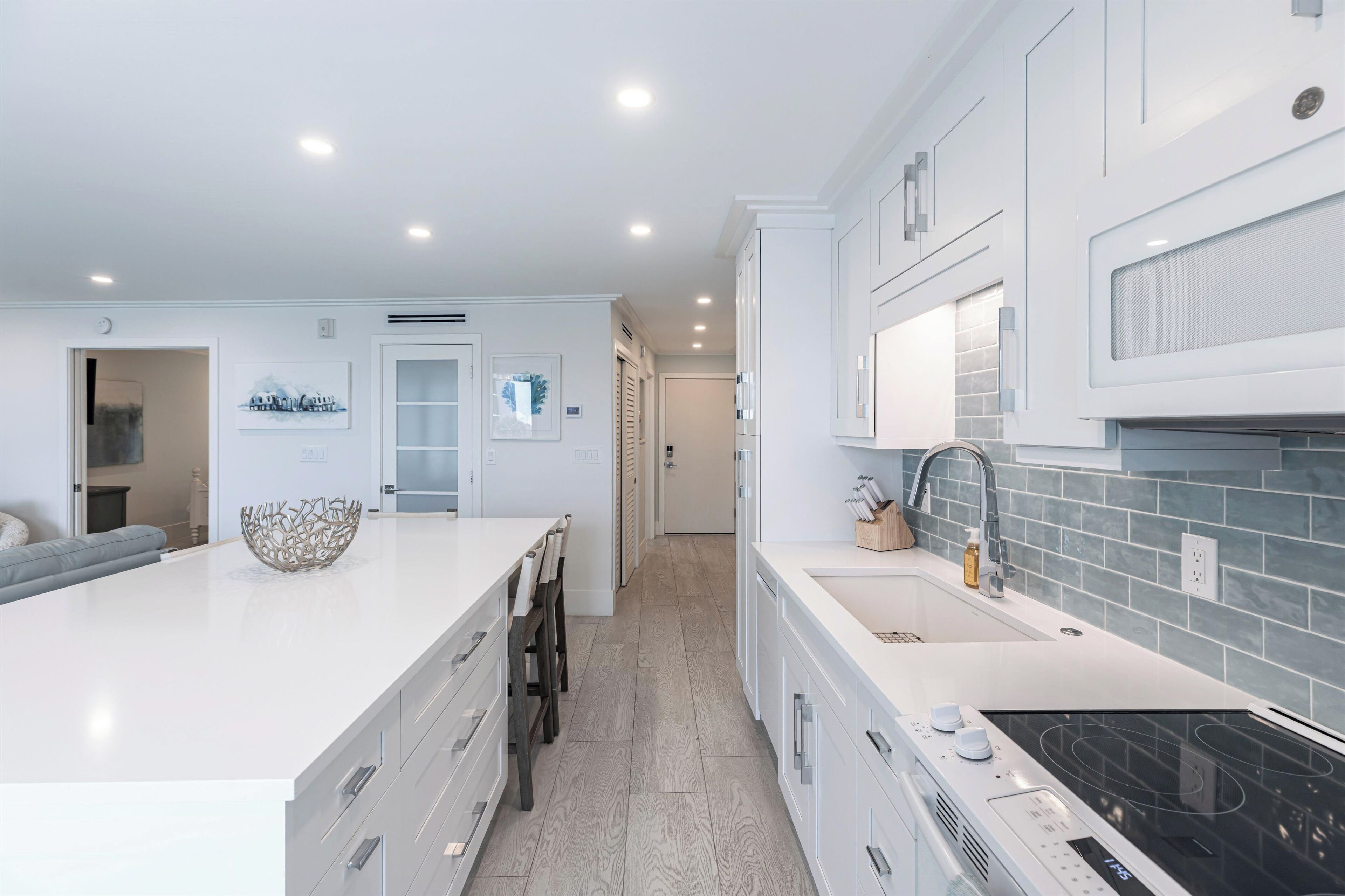 A modern kitchen with white cabinetry, a large island, and a black induction cooktop.
