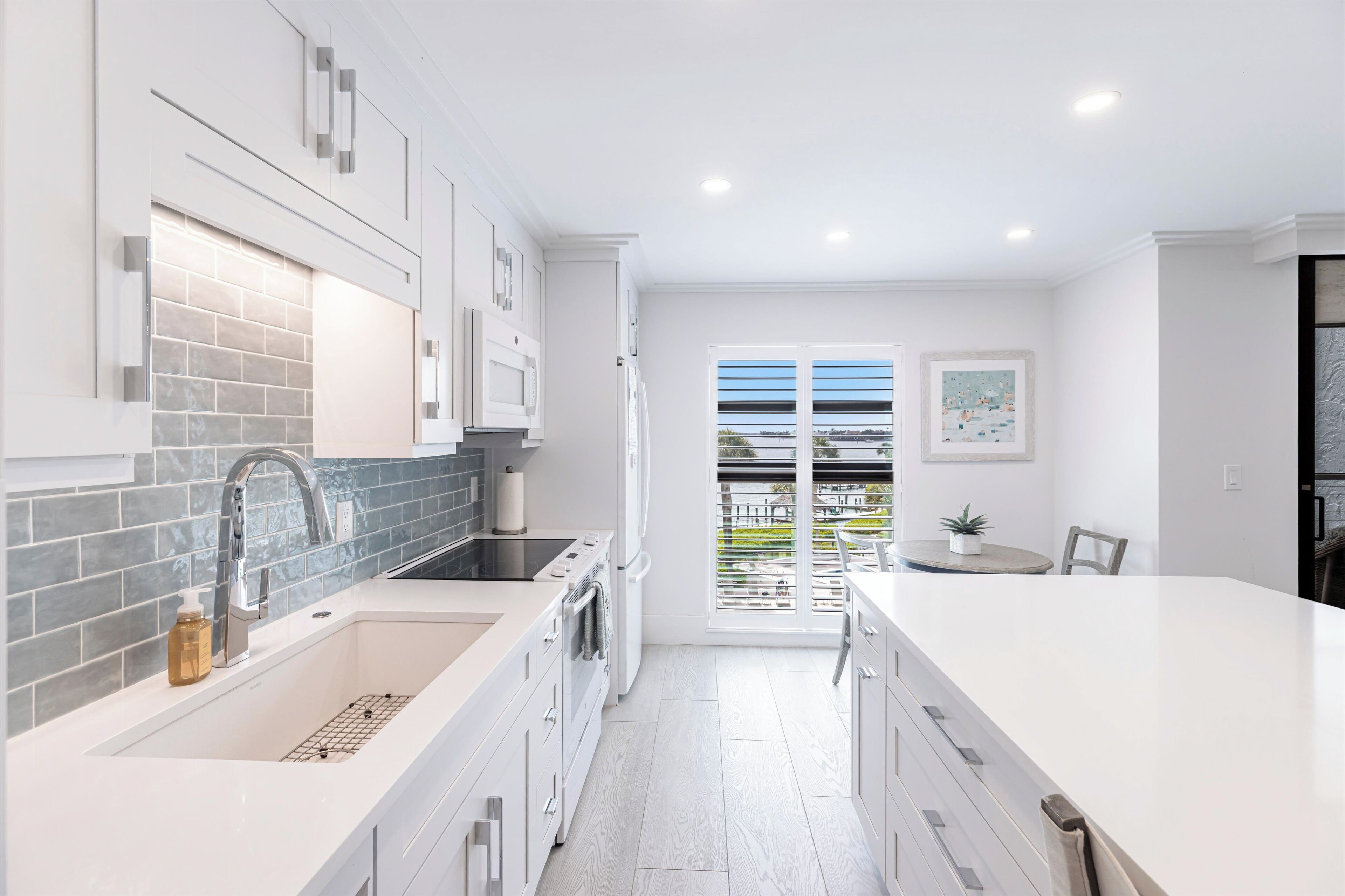A modern kitchen with white cabinets, a grey backsplash, and a large island.