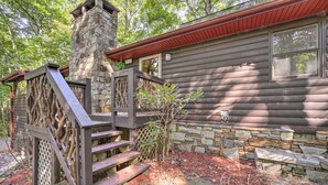 Une cabane dotée d’une cheminée en pierre, d’une terrasse en bois et de murs en pierre.