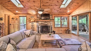 Un intérieur de chalet chaleureux avec une cheminée en pierre, un plafond en bois et de grandes fenêtres.