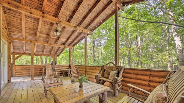 Une terrasse en bois, meublée de façon rustique, avec notamment une table et des chaises, et entourée d’une forêt.
