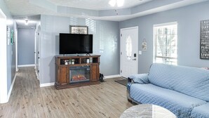 A living room with a fireplace, a television, a ceiling fan, and a large window. - Above-ground Pool & Backyard at Murfreesboro Home! (Murfreesboro)