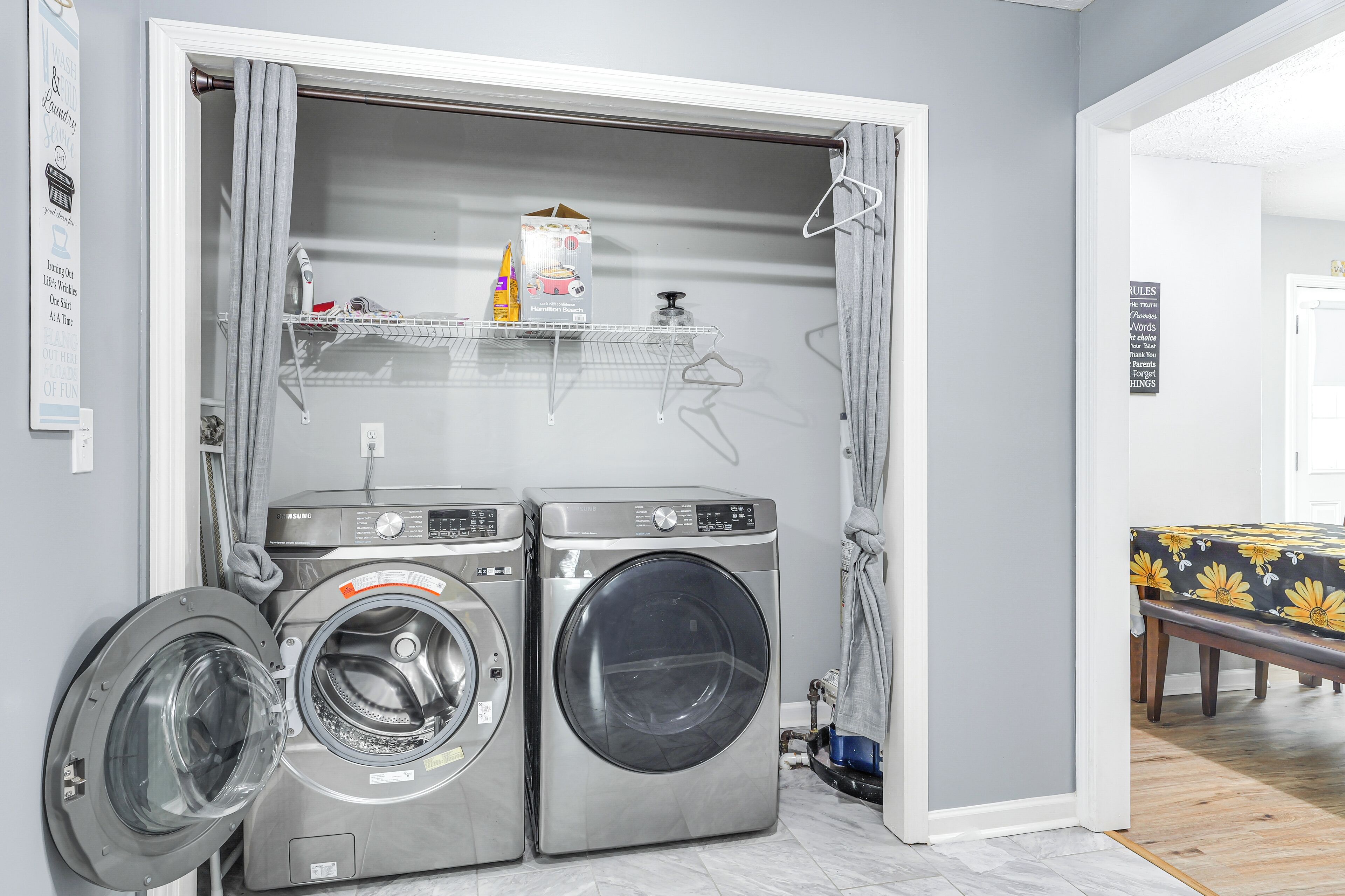 A laundry room with two front-loading washing machines, a drying rack, and a shelf with laundry supplies.