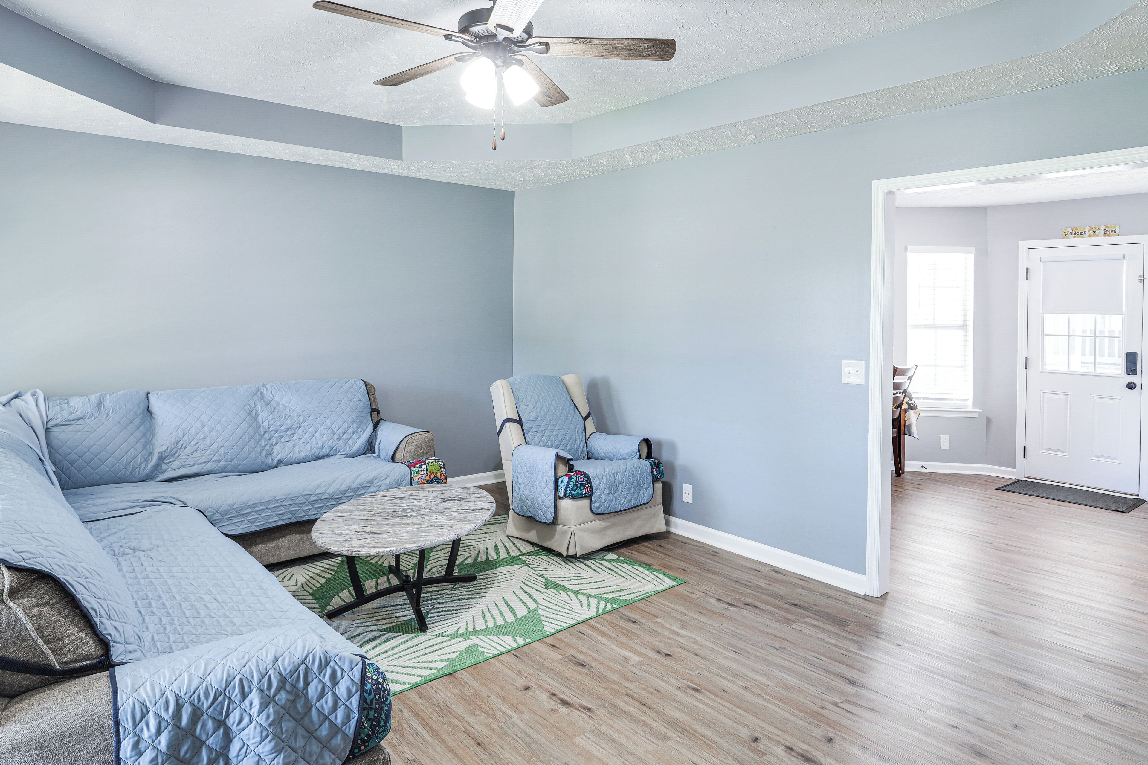 A living room with a sectional sofa, a chair, a coffee table, and a ceiling fan.