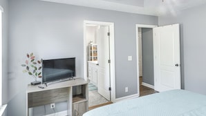 A bedroom with a bed, a TV on a wooden stand, and a door leading to a bathroom. - Above-ground Pool & Backyard at Murfreesboro Home! (Murfreesboro)