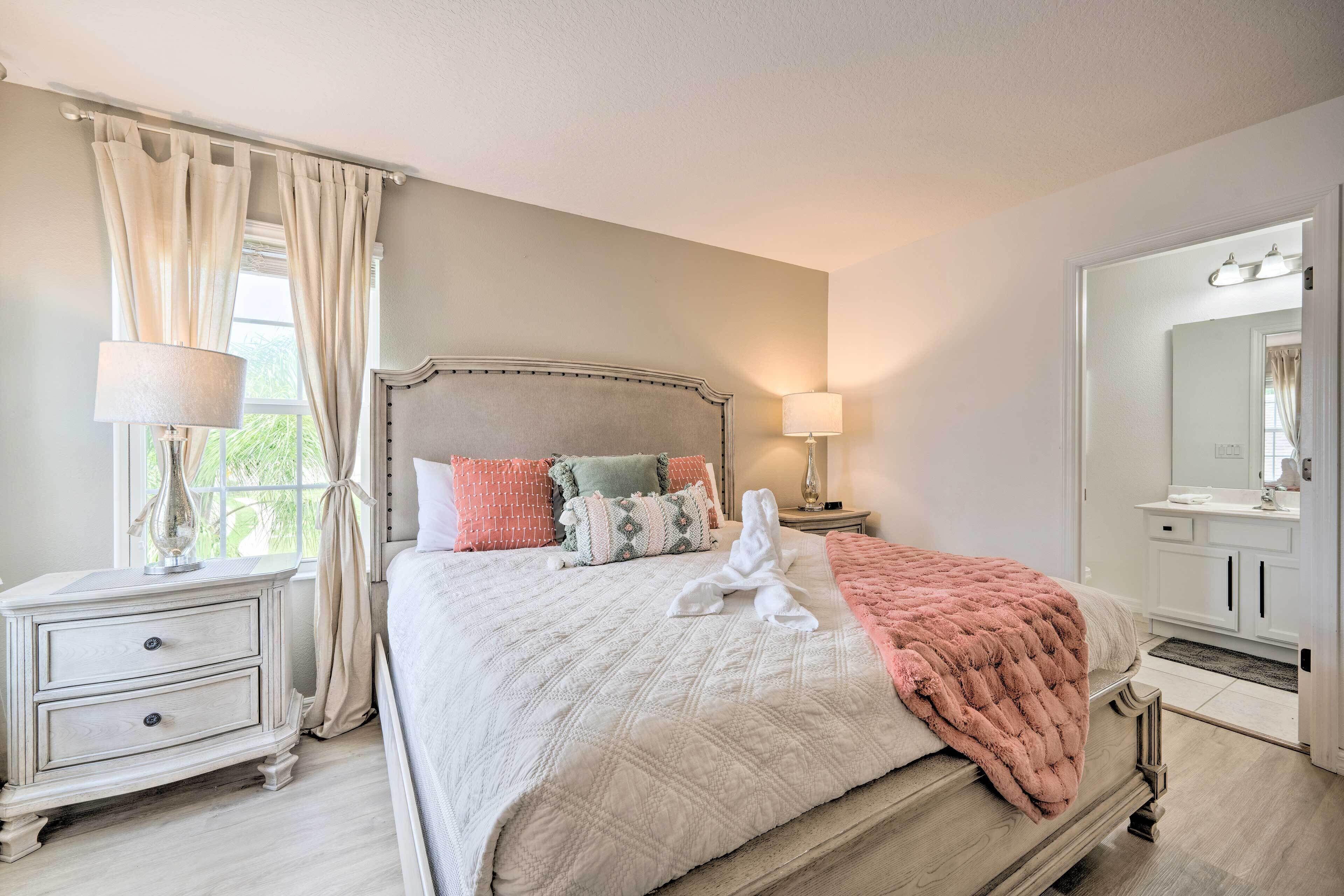 Quarto com cama, mesas de cabeceira, penteadeira, espelho e janela com cortinas.