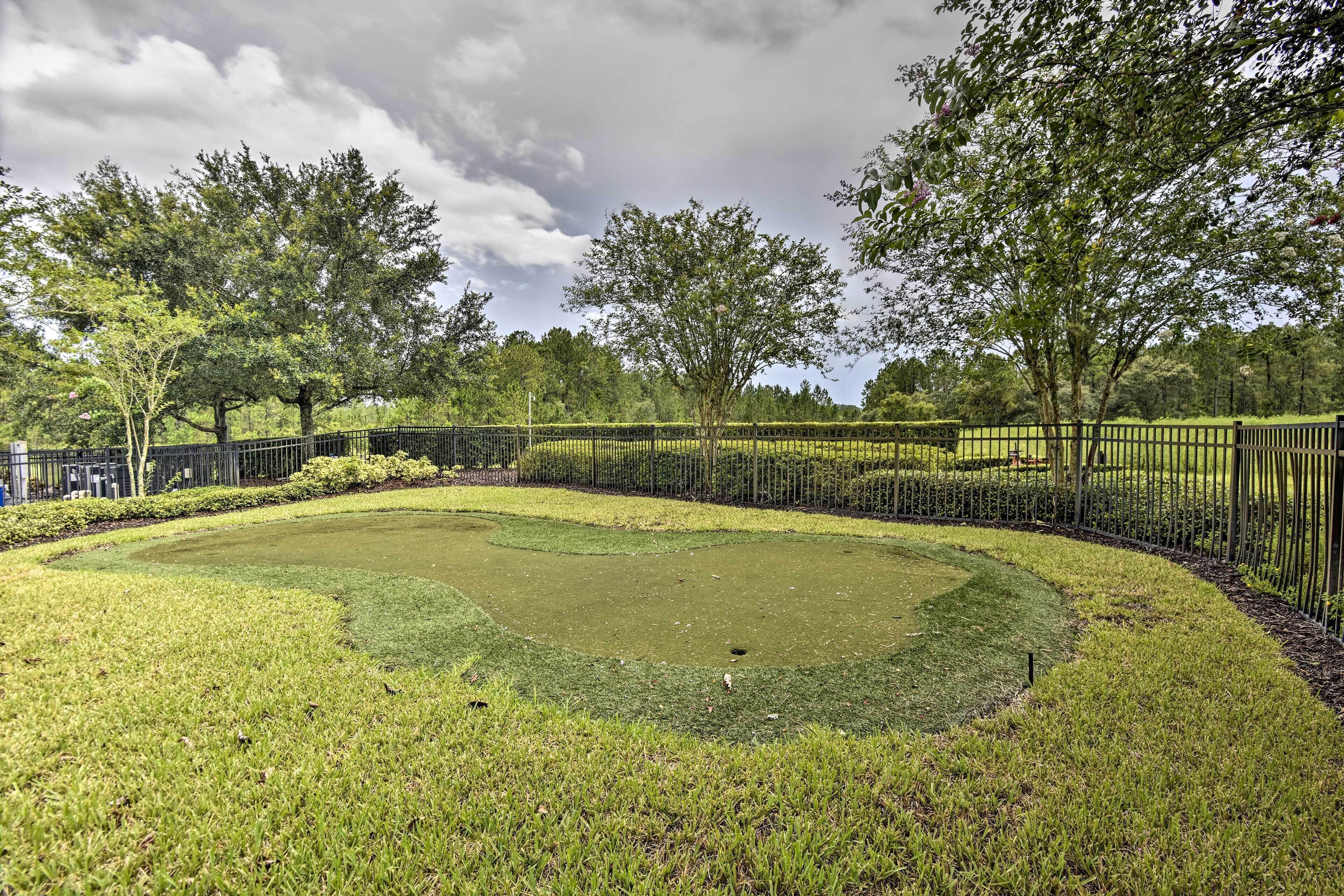 Un terrain de golf bien entretenu, doté d’un green d’entraînement, entouré d’une clôture métallique et d’une végétation luxuriante.