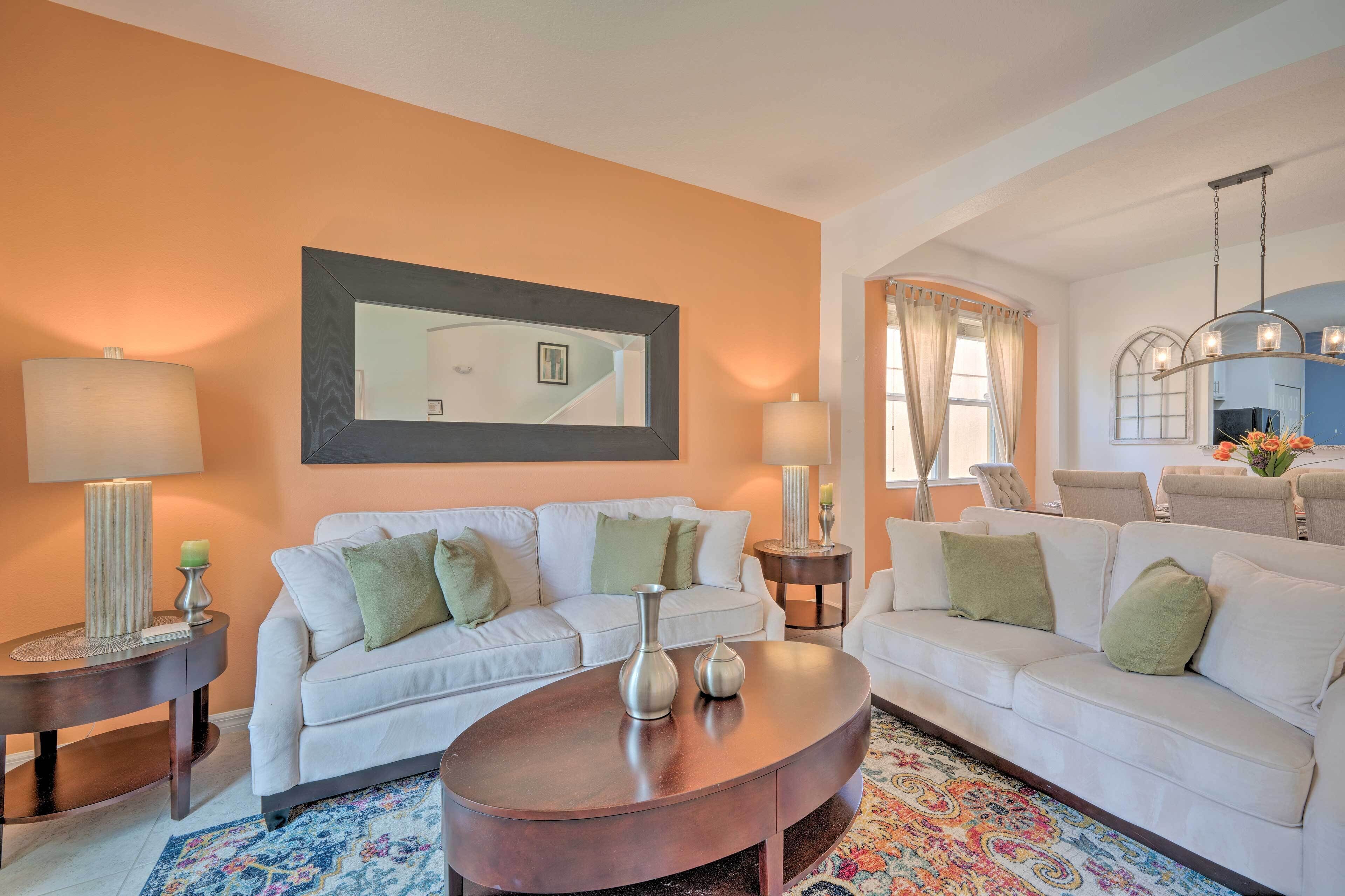 A living room with two white sofas, a coffee table, a mirror, and a chandelier.