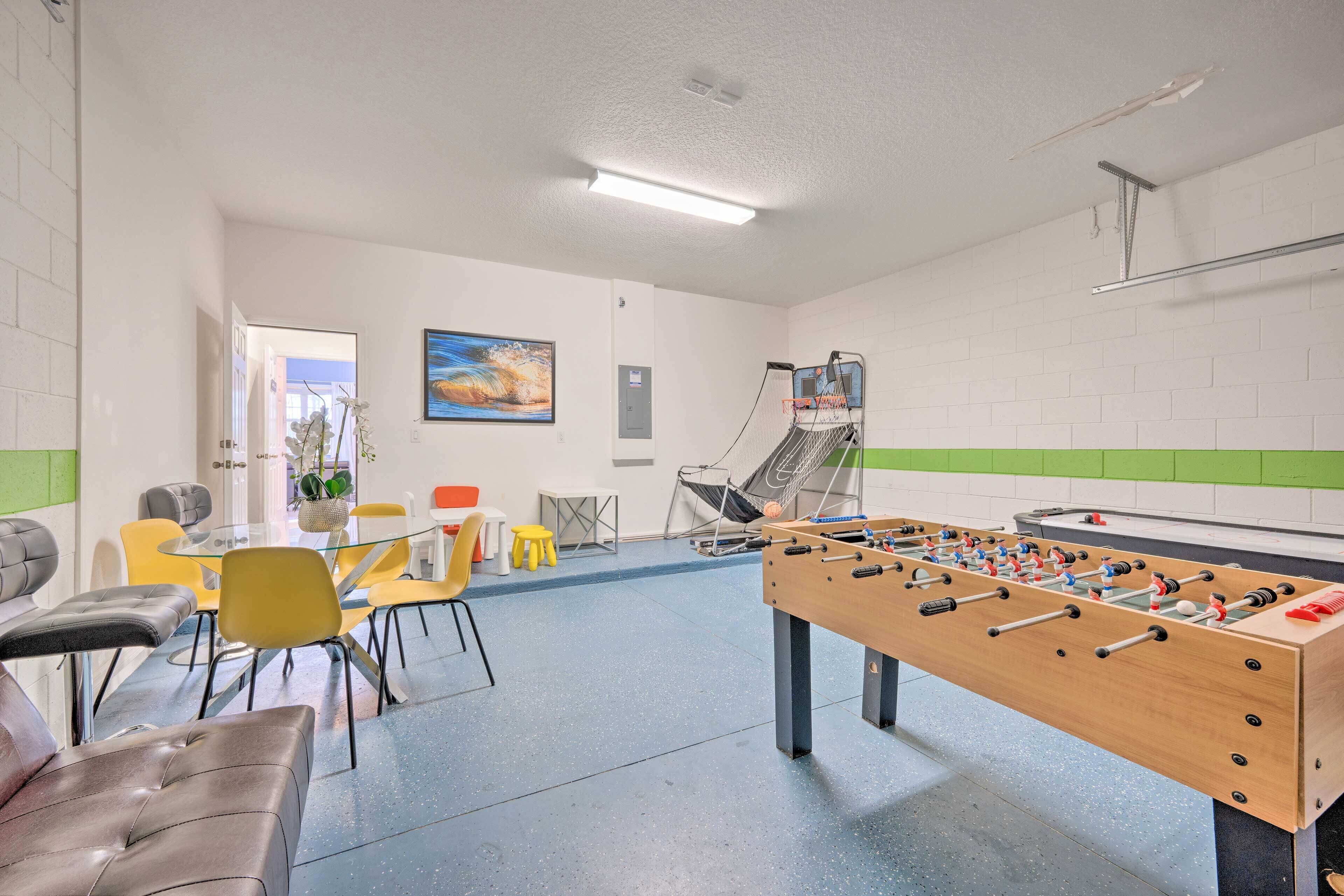 A room with a foosball table, a sofa, and a dining area with chairs and a table.