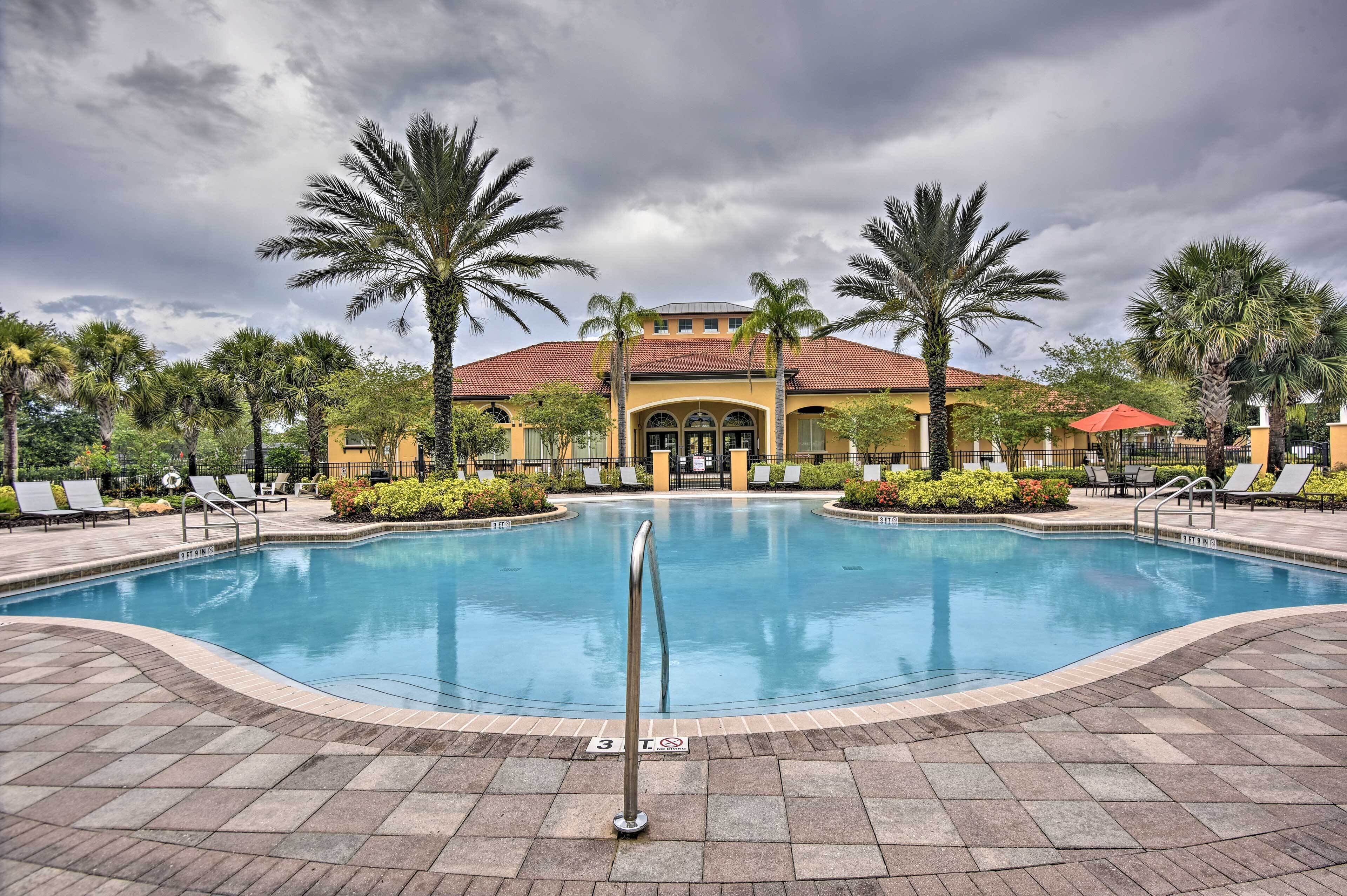 A swimming pool with lounge chairs and palm trees, surrounded by a building with a tiled roof.