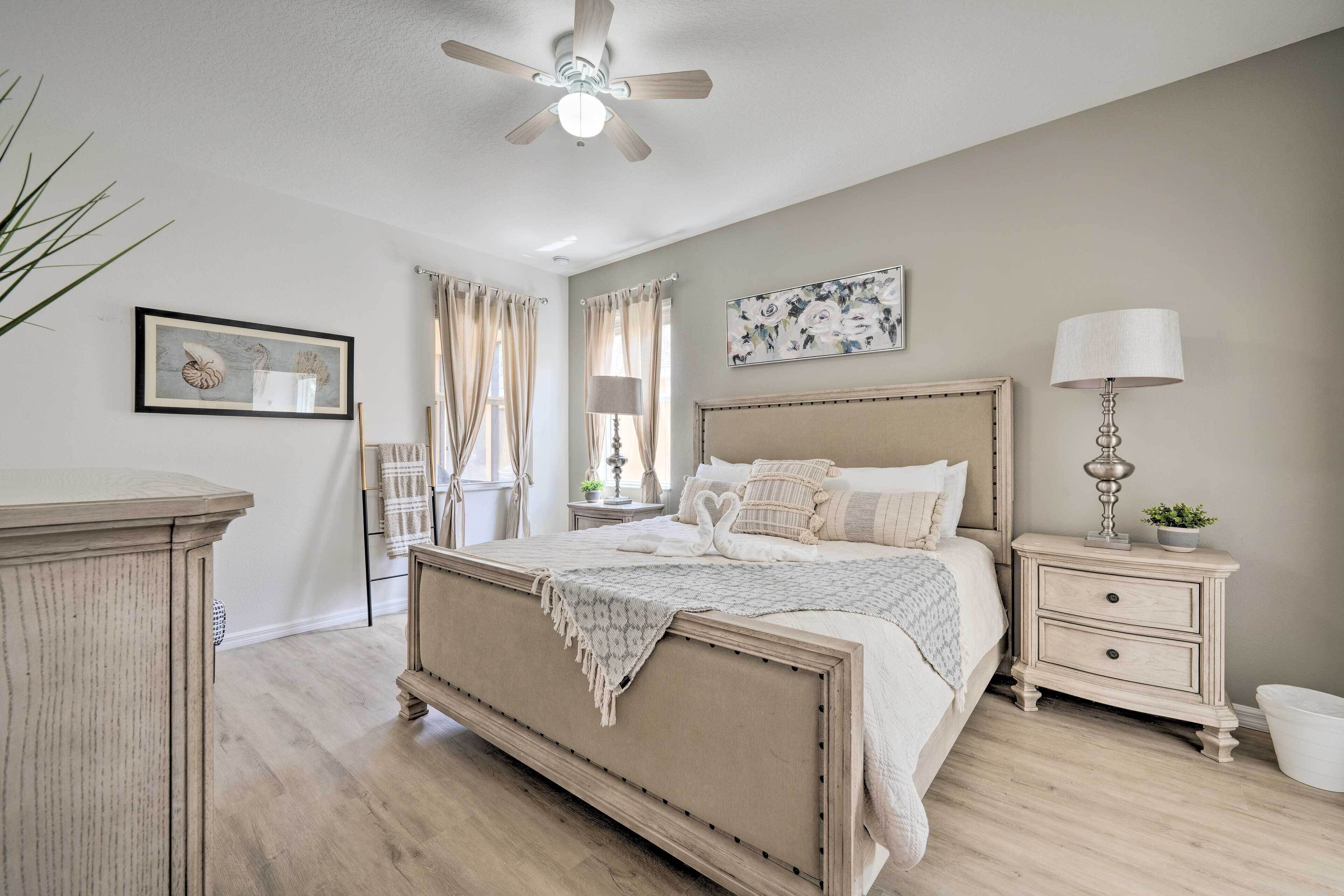 A bedroom with a large bed, a nightstand, a ceiling fan, and a window with curtains.