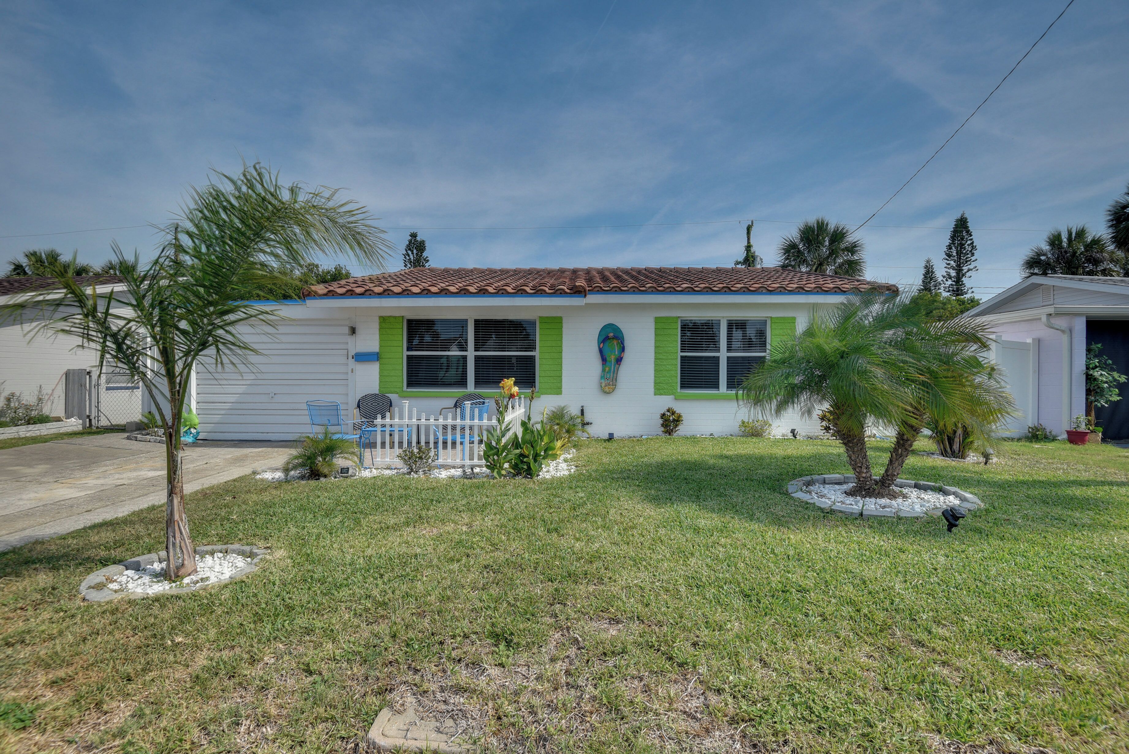 A single-story house with a tiled roof, green shutters, and a small front yard with a palm tree and a circular garden bed.