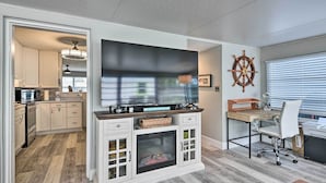 A modern kitchen with white cabinetry, a built-in fireplace, and a large flat-screen TV. - Pet-friendly Ormond Beach Home w/ Fire Pit! (Ormond Beach)