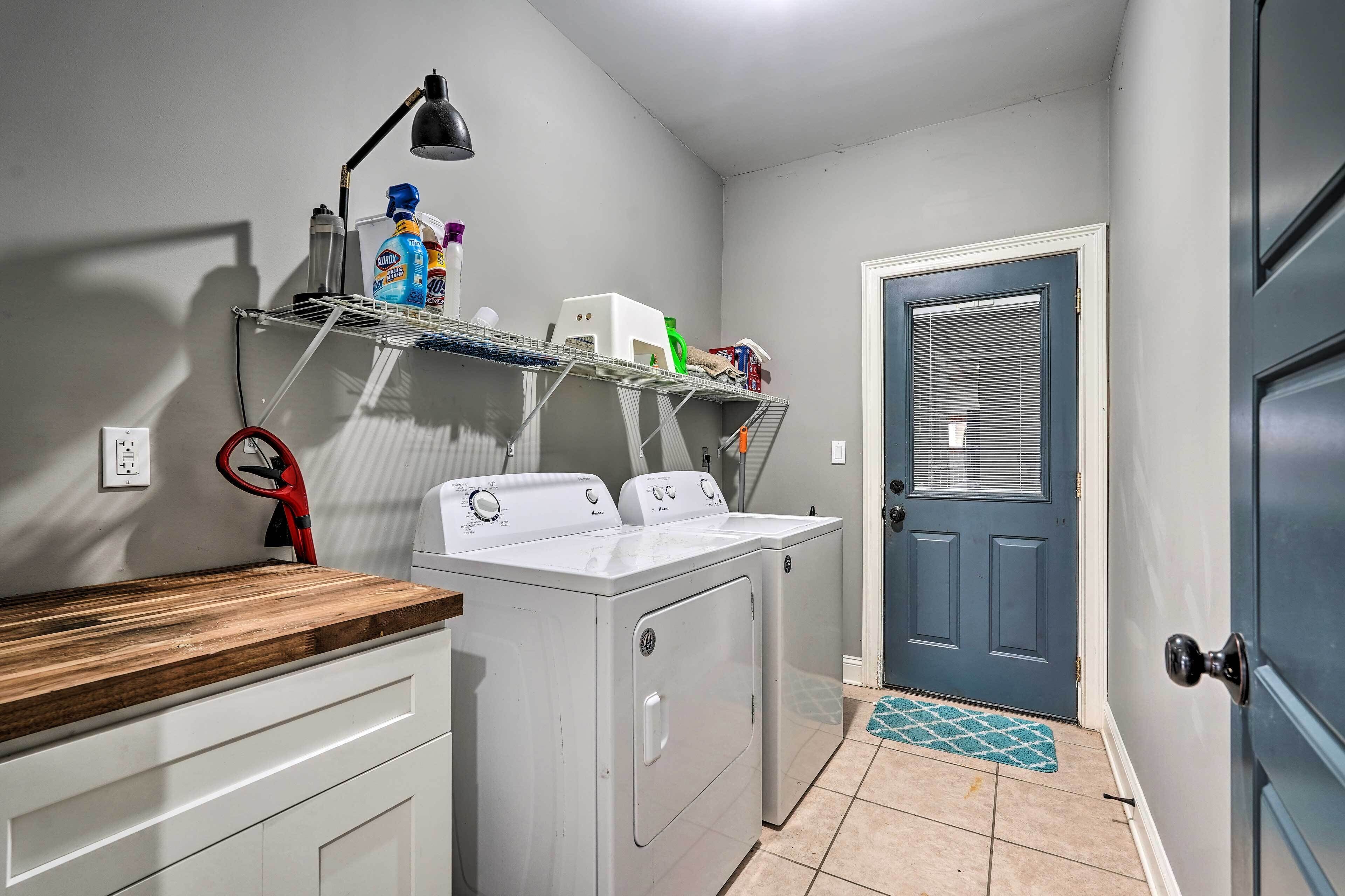 A laundry room with a washing machine, dryer, shelf with cleaning supplies, and a door with a window.