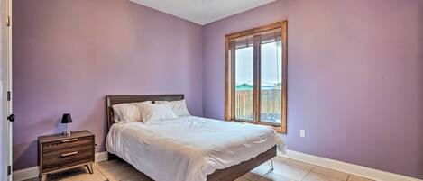 A bedroom with a bed, nightstand, and a window with a view.