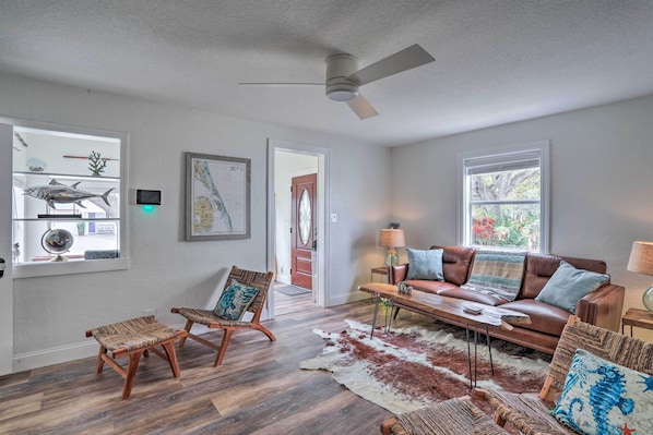 A living room with a brown leather sofa, two wooden chairs, a coffee table, and a cowhide rug.