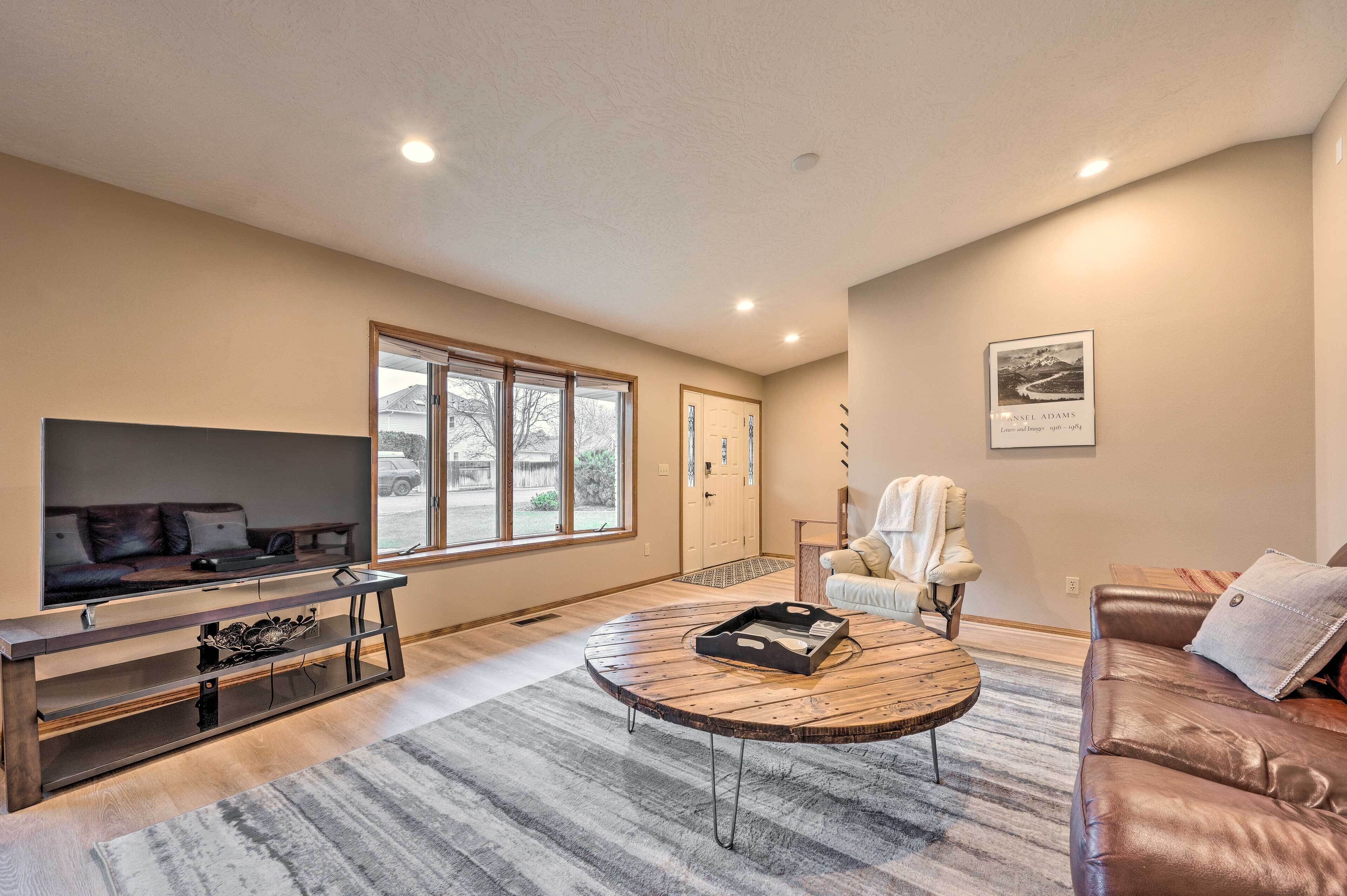 A living room with a flat-screen TV, a wooden coffee table, a leather sofa, and a large window.
