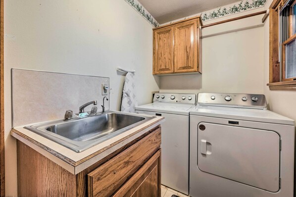 Une cuisine compacte comprenant un évier, des placards en bois, une cuisinière et un lave-linge.