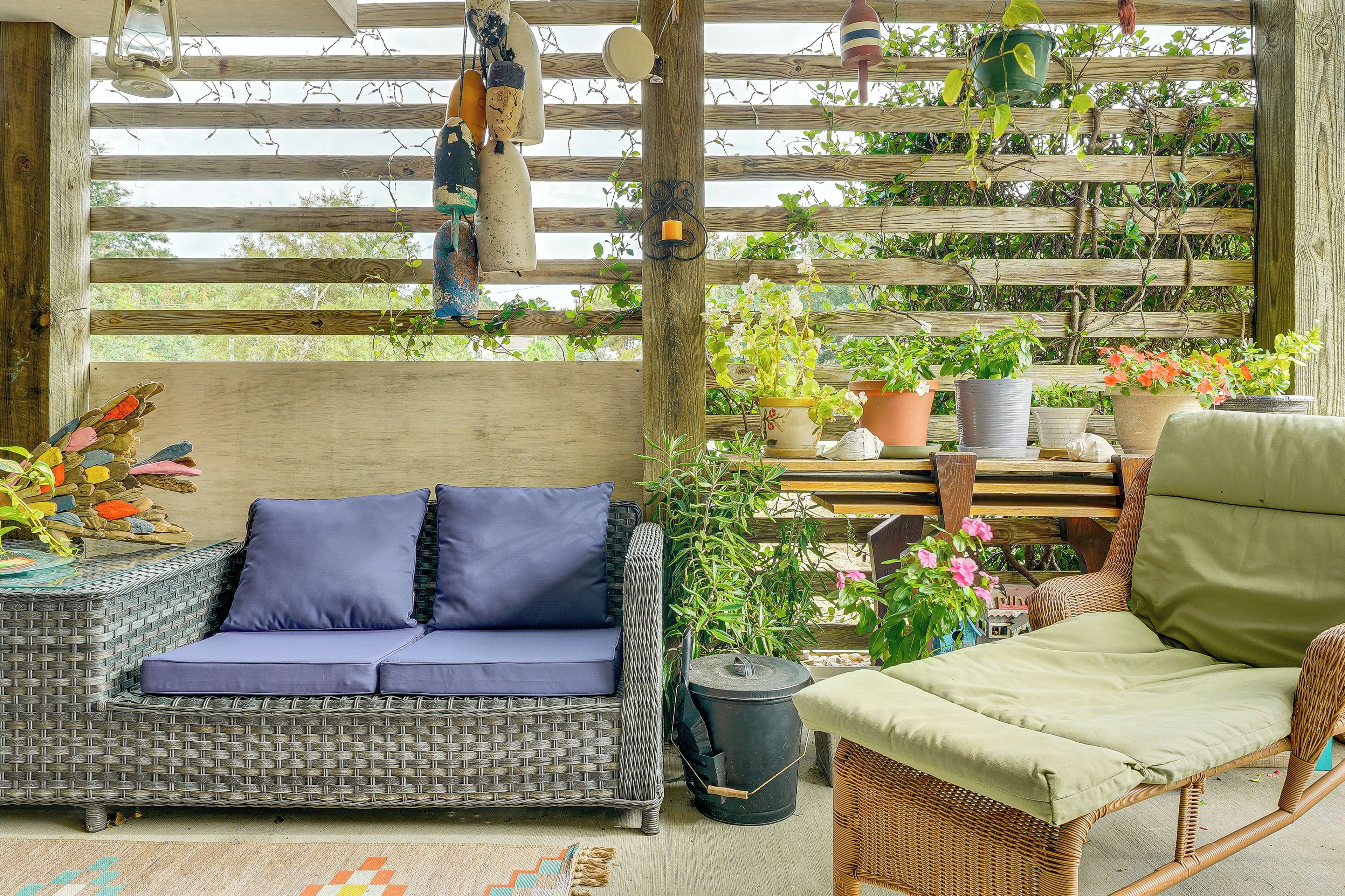 Un sofá de mimbre con cojines azules, una silla de mimbre con un cojín verde y varias plantas en macetas.