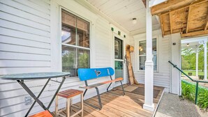 A covered porch with a wooden bench, a small table, and a blue object resembling a surfboard. - Rustic & Historic Guildhall Farmhouse w/ Fire Pit! (Guildhall)