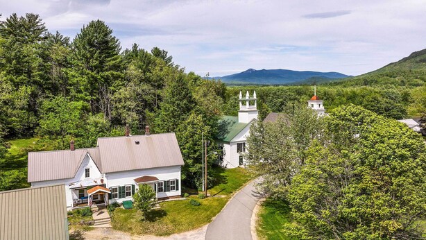 A white church with a bell tower and a green roof, surrounded by dense forest and hills in the background. - Rustic & Historic Guildhall Farmhouse w/ Fire Pit! (Guildhall)