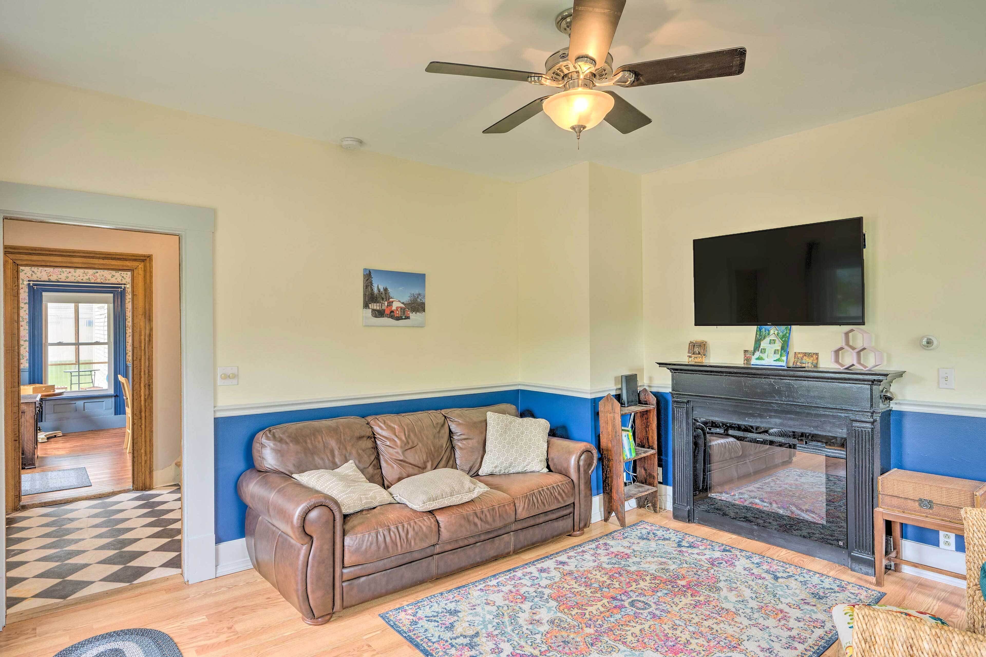 A living room with a brown leather sofa, a patterned rug, a fireplace, and a ceiling fan.