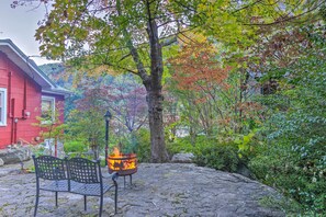 A stone patio with a fire pit and a bench, surrounded by trees with autumn foliage.