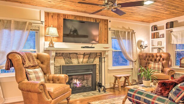 A cozy living room with a fireplace, leather armchairs, a plaid sofa, and a television mounted above the fireplace. - Mtn Views + Fire Pit: Serene Chimney Rock Abode (Chimney Rock)