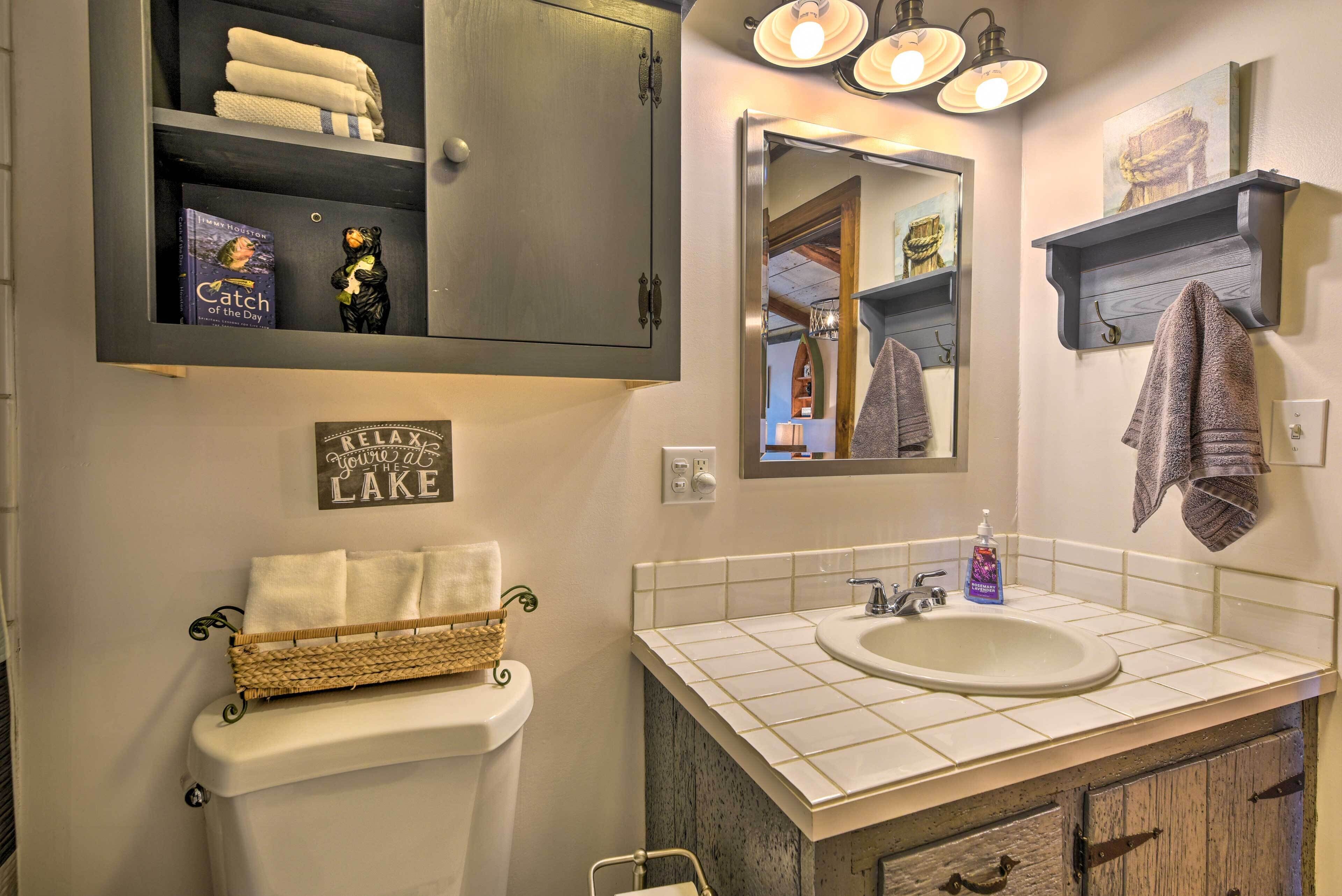 A bathroom with a white sink, a mirror, a towel rack, and a cabinet with towels.