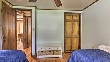 A room with two beds, wooden floors, a white dresser, and a wooden door.