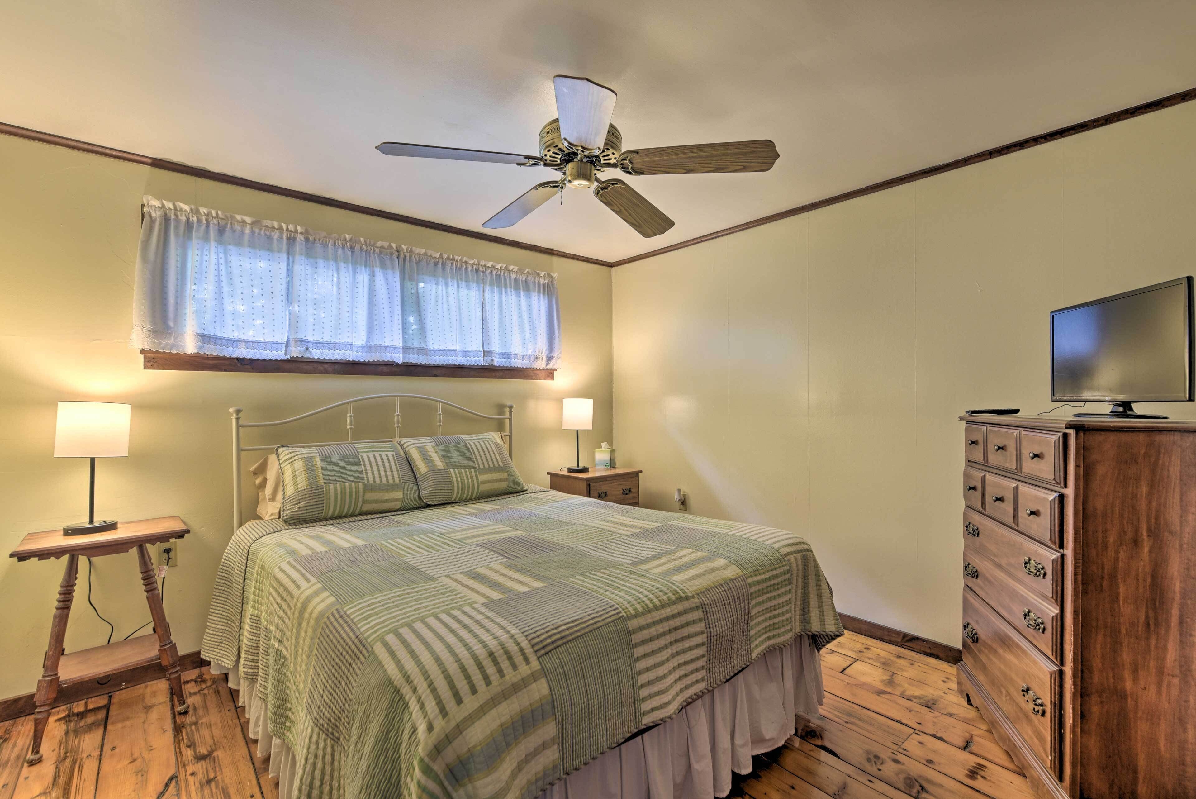 A bedroom with a bed, bedside lamps, a wooden dresser, and a ceiling fan.