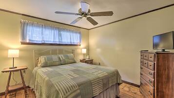 A bedroom with a bed, bedside lamps, a wooden dresser, and a ceiling fan.