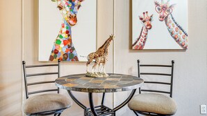 A dining area with a round table and two chairs, a decorative giraffe sculpture, and two framed giraffe paintings on the wall. - Granbury Studio - 10 Mins From Town + The Lake! (Granbury)