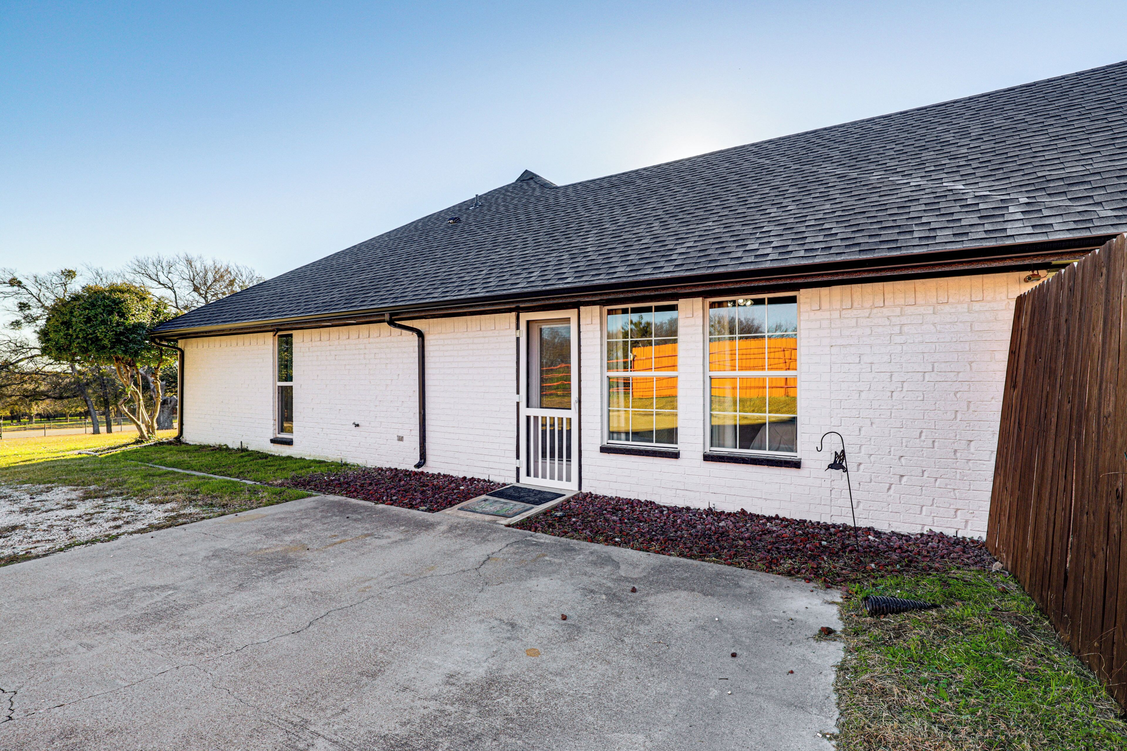 A single-story house with a white brick exterior, a dark roof, and a front door with a small porch.