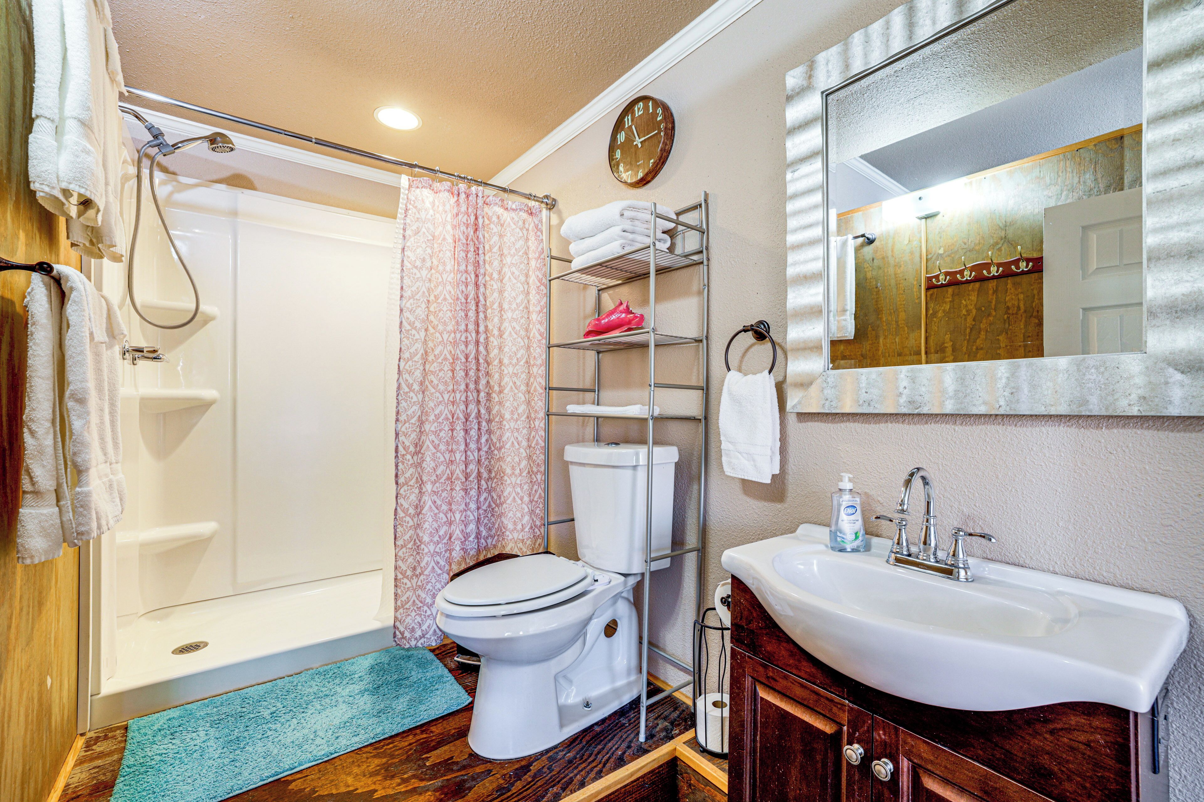 A bathroom with a shower, toilet, sink, and a clock on the wall.