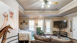 A hotel room with a bed, a sofa, a TV, and a ceiling fan. - Granbury Studio - 10 Mins From Town + The Lake! (Granbury)