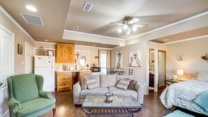 A cozy living room with a green armchair, a sofa with patterned cushions, a coffee table, and a ceiling fan. - Granbury Studio - 10 Mins From Town + The Lake! (Granbury)