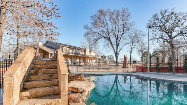 A swimming pool with stone steps leading up to a building with a sloped roof. - Kingston Home w/ Pickleball: Steps to Lake Texoma! (Kingston)