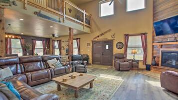 A spacious living room with a large sectional sofa, a wooden coffee table, and a fireplace. There is a balcony with a railing and a ceiling fan.