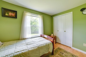 A bedroom with a bed, a window with curtains, a nightstand, a wardrobe, and a clock on the wall.