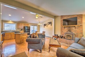 A spacious living area with a fireplace, a kitchen with wooden cabinets, and a dining area with a large window. - Quiet Catskills Getaway w/ Deck & Mtn Views (New Kingston)