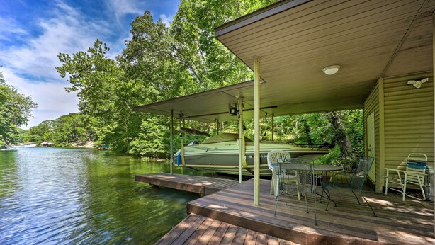 A wooden dock extending into a calm lake, with a covered seating area and a boat docked nearby. - Lakefront Getaway w/ Private Dock & Kayaks! (Bella Vista)