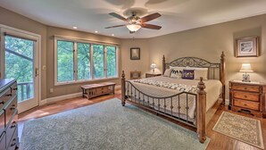 A bedroom with a large bed, a ceiling fan, a nightstand, a dresser, and a window with a view of trees.